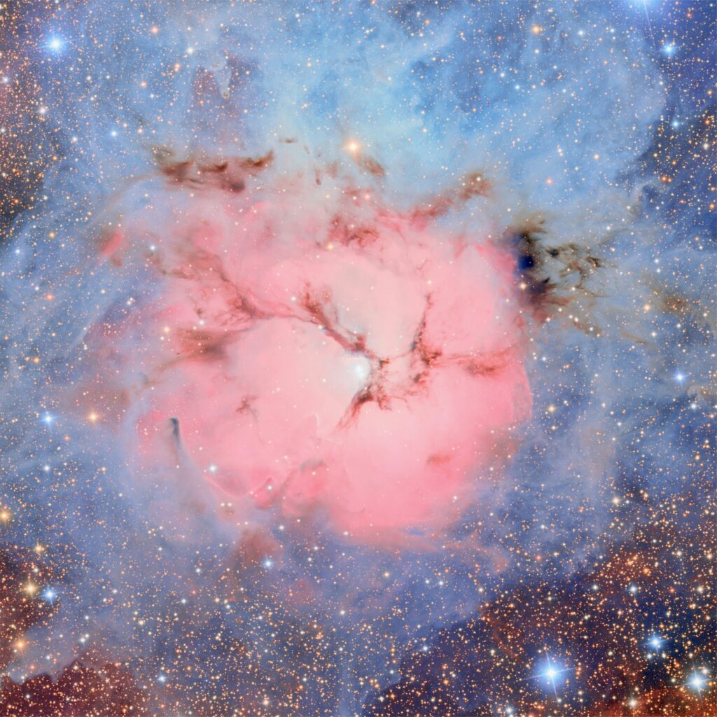 The star-forming Trifid Nebula, also known as Messier 20, as imaged by NSF–DOE Vera C. Rubin Observatory. The Trifid Nebula is an unusual combination of an open cluster of stars, an emission nebula (the pink region), a reflection nebula (the blue region), and a dark nebula (the dark regions)
