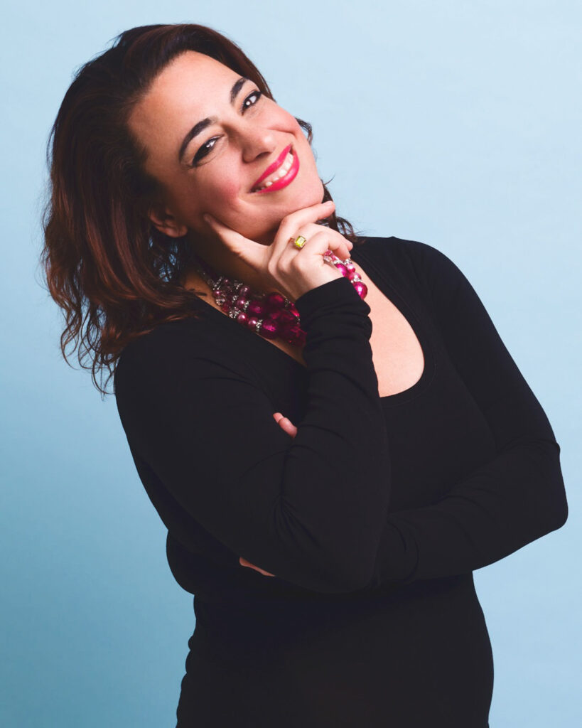 A headshot of Sara Roccisano smiling wearing a black sweater and pink beaded necklace.