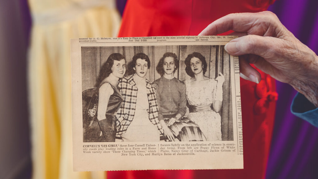 Peggy Dunlop's hand holds an old photo from a newspaper of her and three friends playing leading roles in a variety show at Cornell.