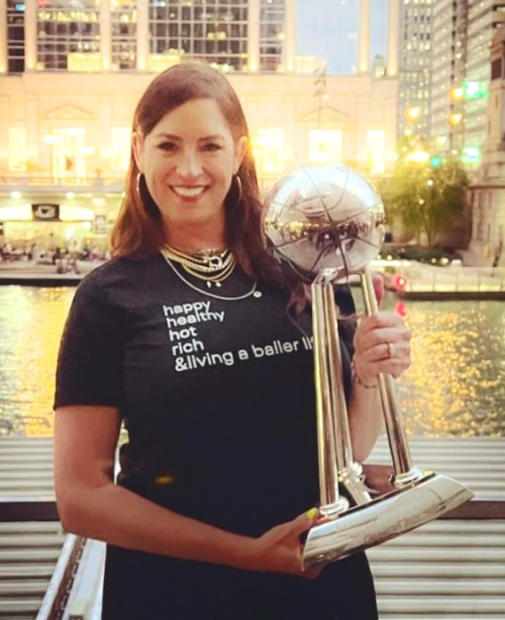 Sarah Spain holds the WNBA Championship trophy up while wearing a shirt that says, "happy, healthy, hot, rich, & living a baller life."