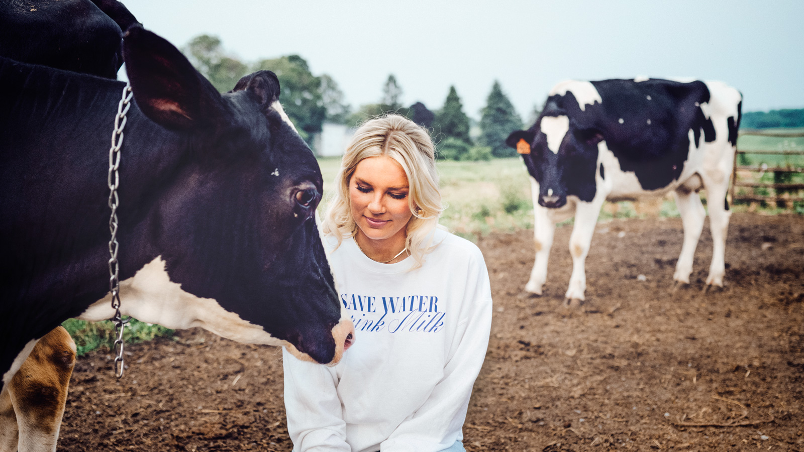 Hailey Pipher with a cow in a pasture, wearing a shirt that says "save water, drink milk."