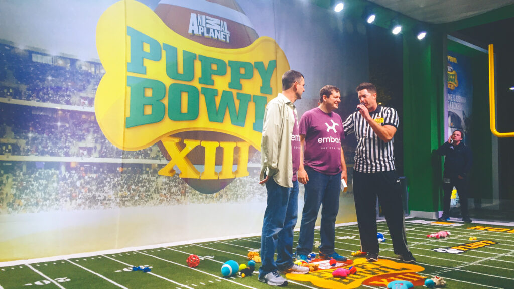 Adam Boyko and his brother wearing Embark shirts with a referee announcer during Animal Planet's Puppy Bowl.