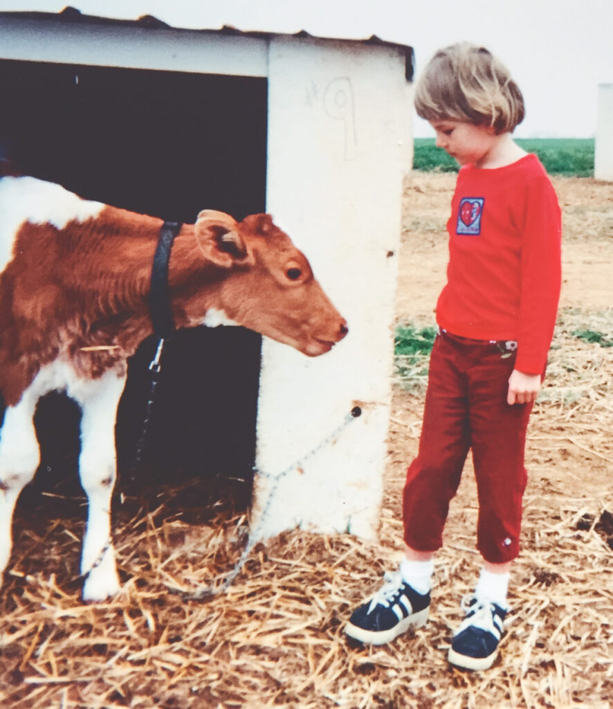 A young Hailey Pipher and a calf look at each other while standing on hay outdoors.