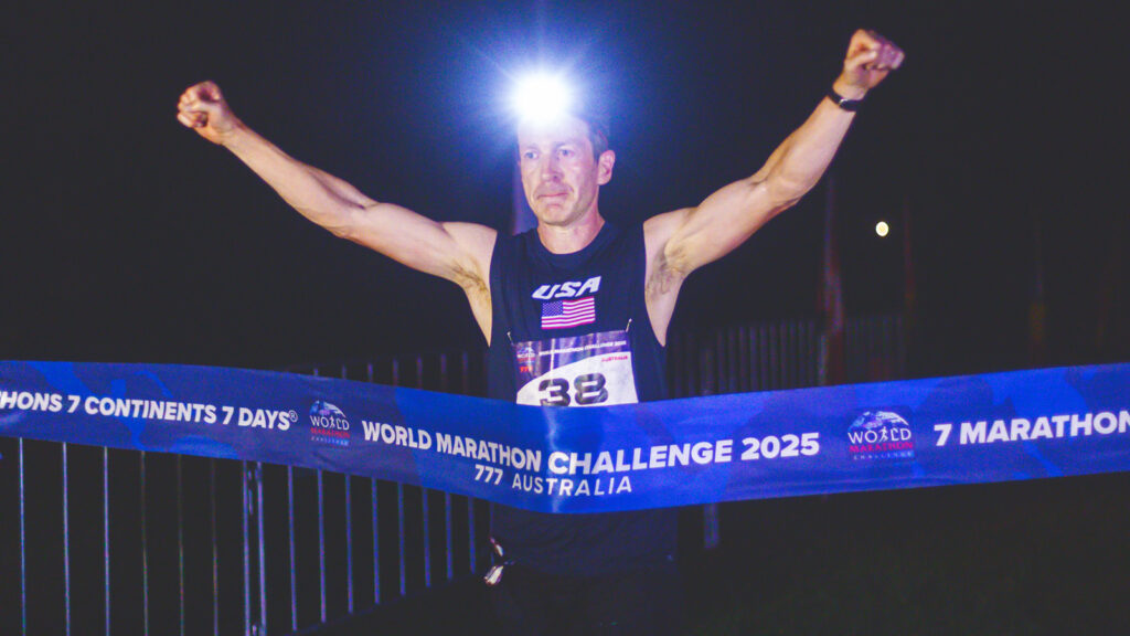Alan Nawoj holds his fists in the air as he crosses the finish line in Australia in the dark with a headlamp shining.