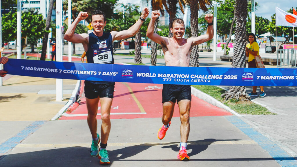 Alan Nawoj and another runner raise their hands in the air and smile while crossing the finish line together in South America.