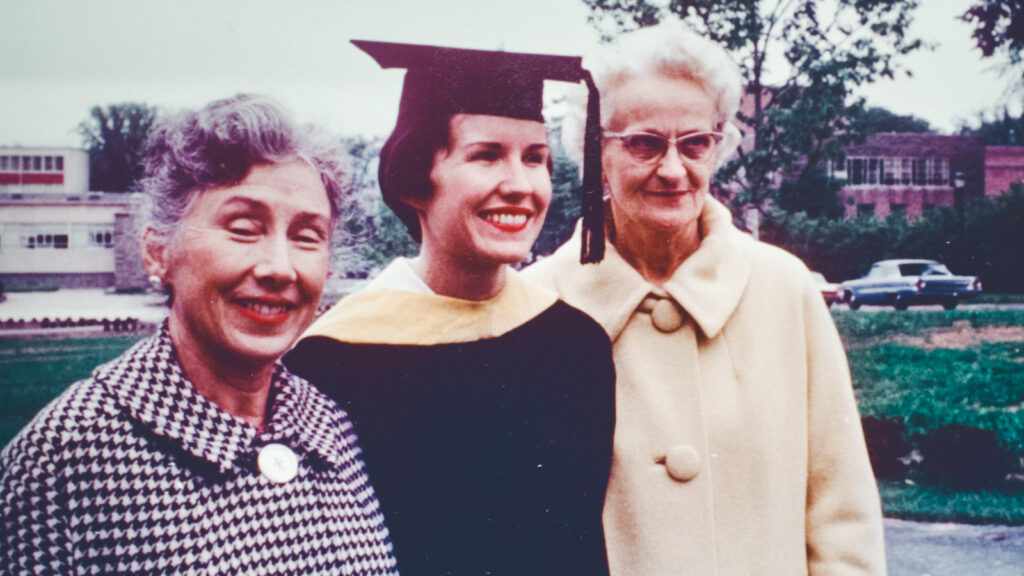 Peggy Dunlop smiles photo a photo with her mother and mother-in-law while wearing her cap and gown during commencement.