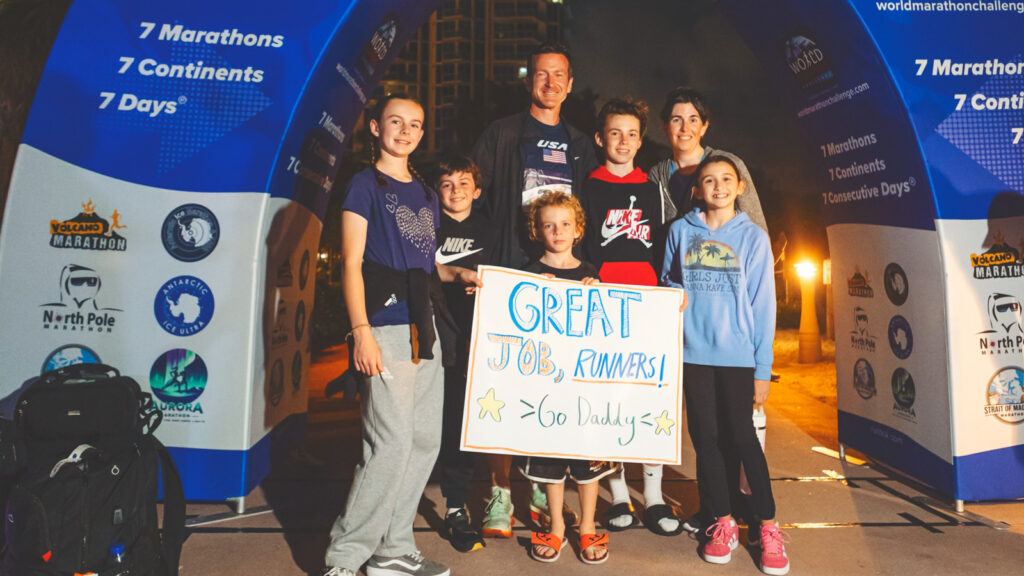 Alan Nawoj with his five kids and wife who are holding a sign that says, "Great job, runners! Go Daddy," in Miami after completing the challenge.