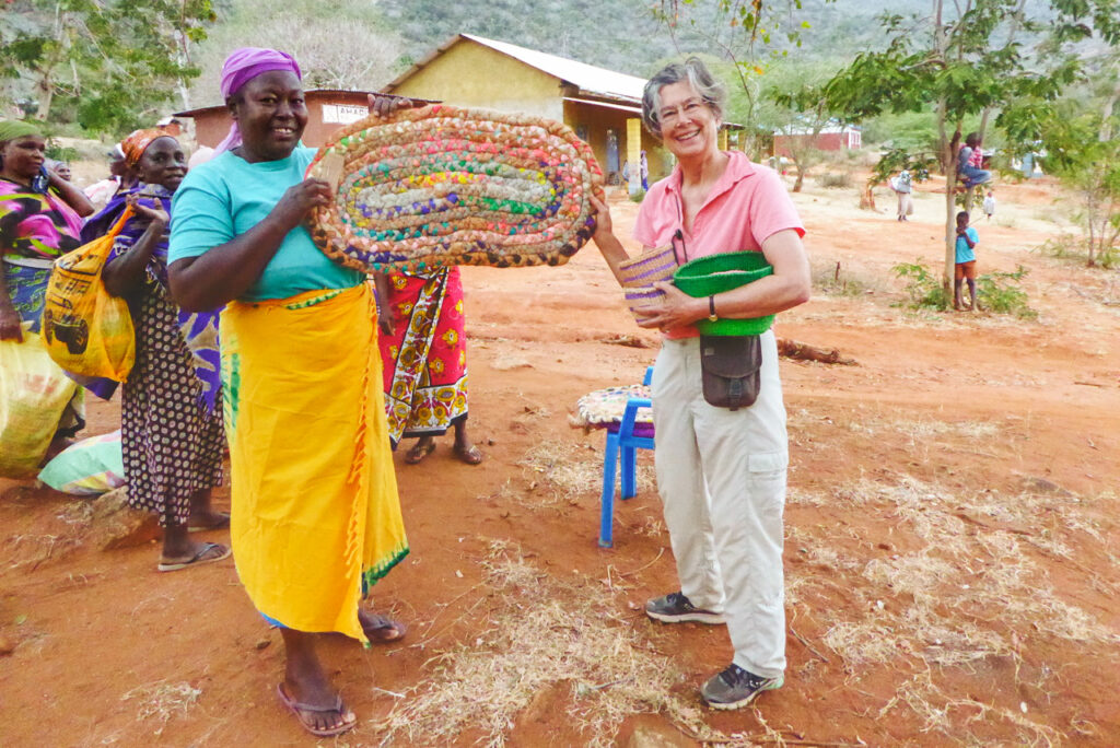 Margaret Higgins Bowker holds up a large colorful basket and smiles with the woman who made it in Kenya.