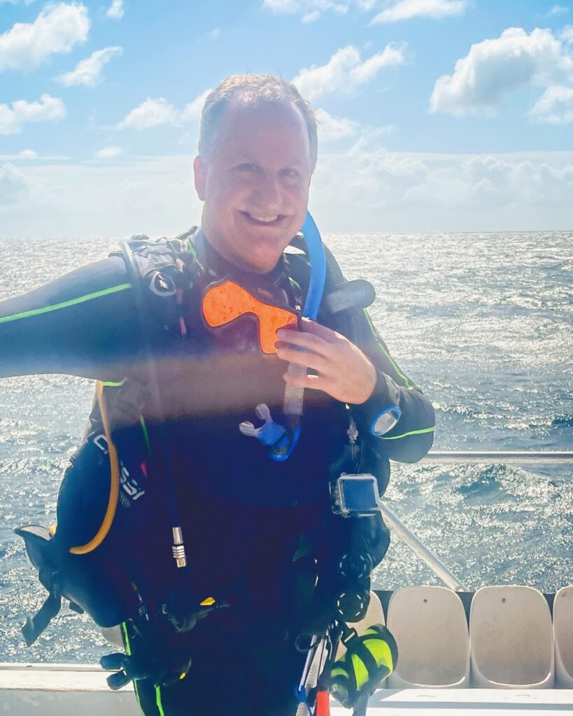 Alan Schussheim on a boat with scuba diving equipment on smiling and preparing for a dive