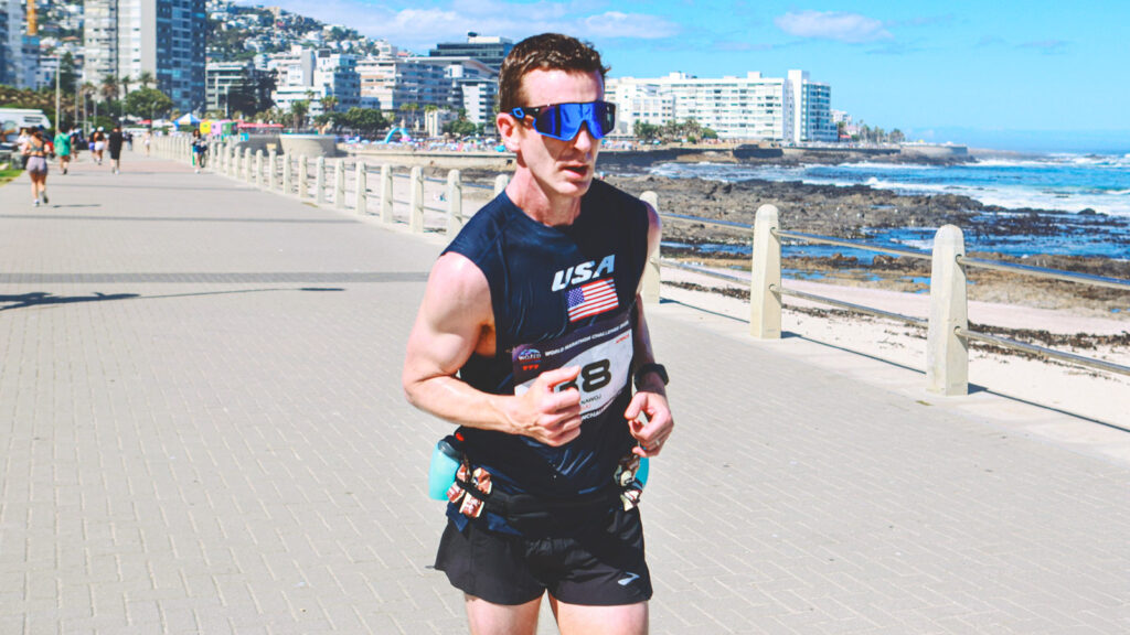 Alan Nawoj runs down a path next to the ocean in Cape Town, South Africa while wearing sunglasses.