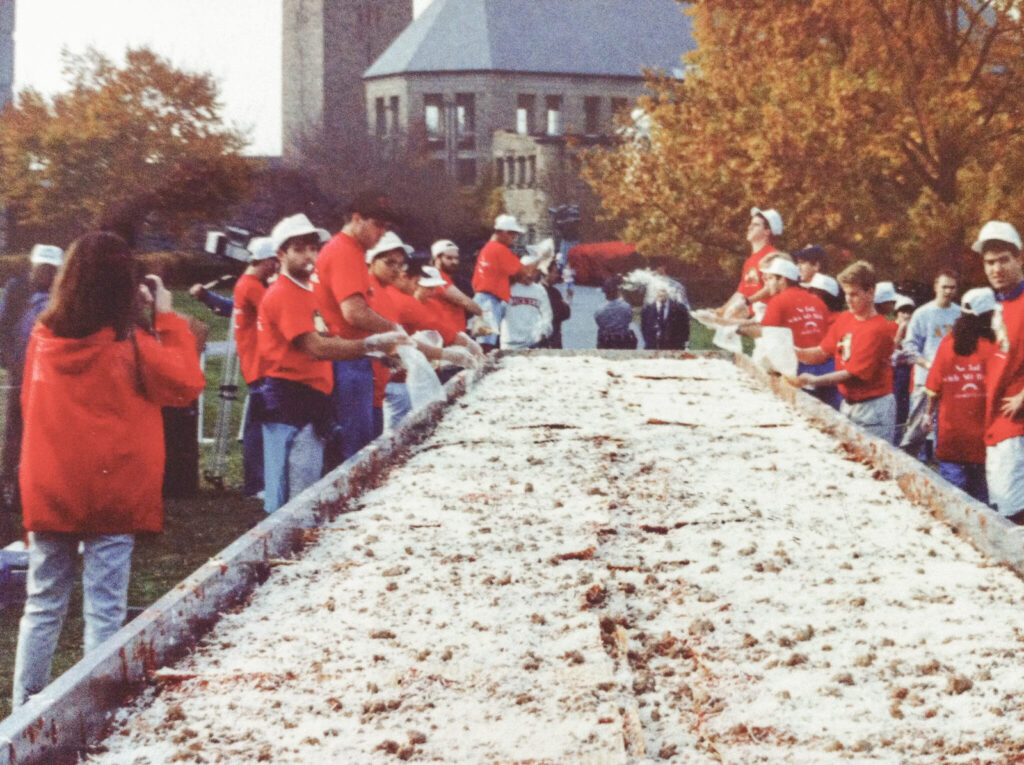 Students gather around the world's largest lasagna in the quad in 1992 while wearing red shirts and white hats.