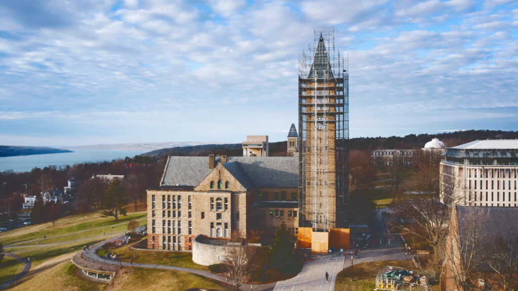 view of McGraw Tower covered in scaffolding during renovations and repair with Uris Library at left and Olin Library to the right