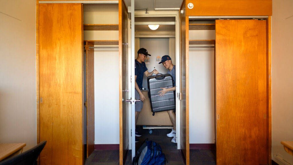 a student and family member move suitcases into a residence hall room during Move-In Weekend, 2025