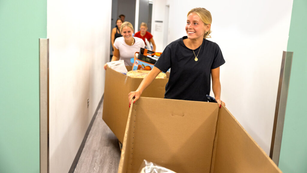a student and family member move wheeled carts in a residence hall during Move-In Weekend, 2025