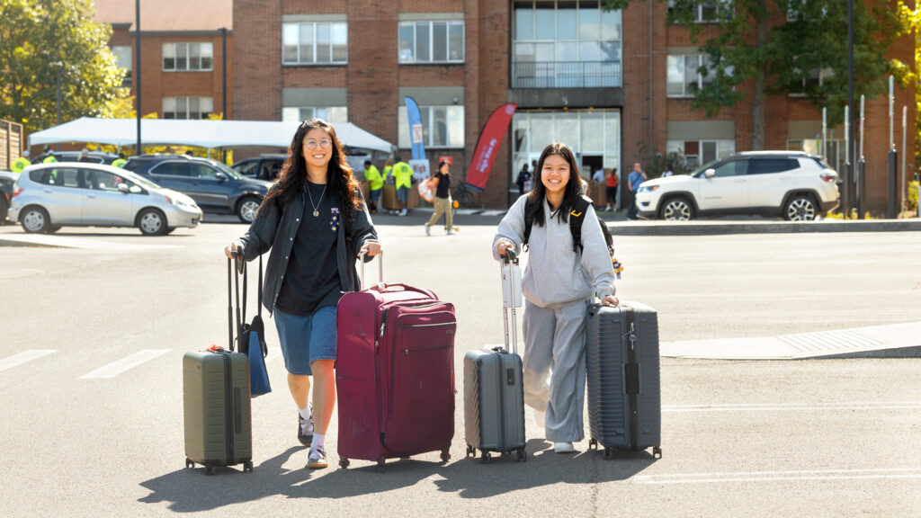 a student and a family member wheel suitcases on campus during Move-In Weekend, 2025