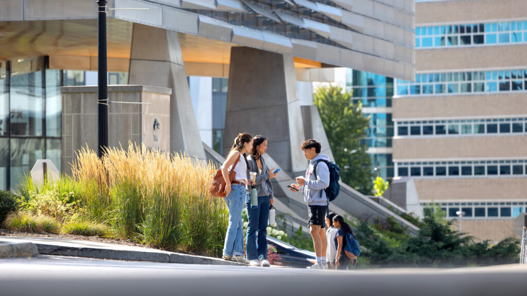 Students chat outside Statler Hall with Gates and Rhodes halls in the background