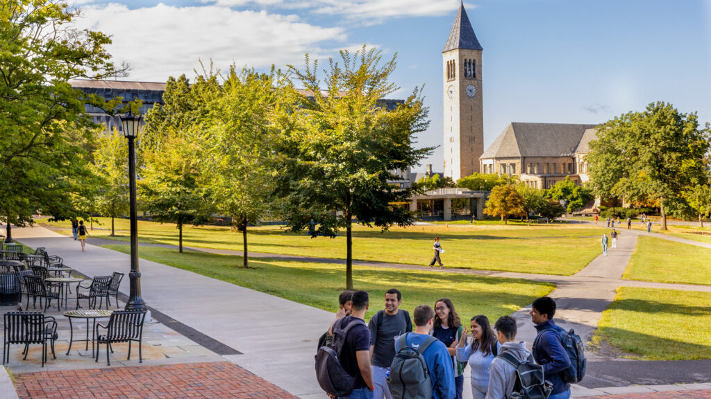 Students stand in a group and talk to each other outside Goldwin Smith Hall with the Arts Quad and clocktower in the background.