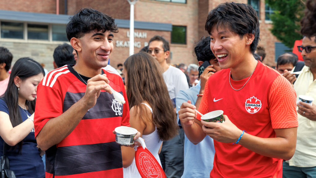 Two students smile and eat ice cream together outside Lynah Rink