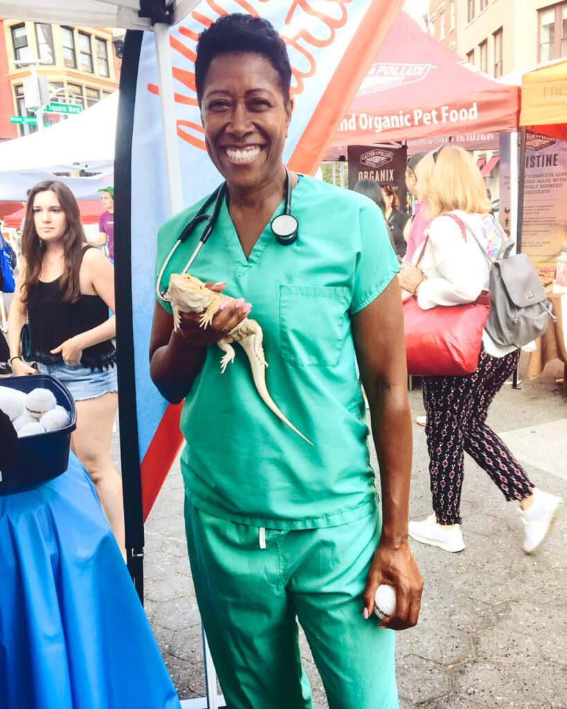 Daphne Mobley in green scrubs with a stethoscope around her neck, holding a lizard and smiling.