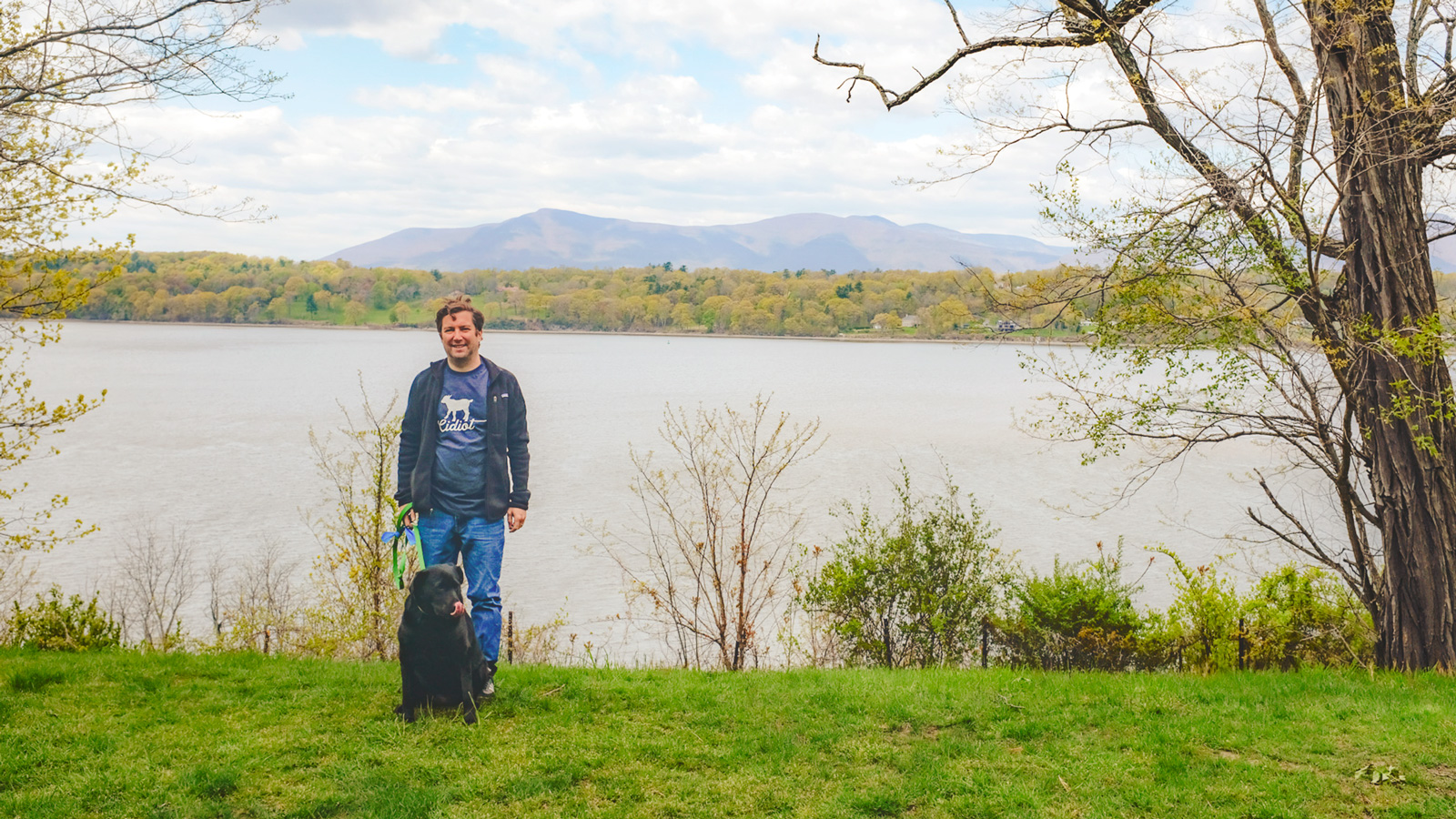Mat Zucker stands by the Hudson River with his dog smiling.