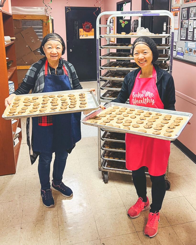 Kimberle Lau and her mother holding trays of cookies in a commercial kitchen in Long Island City.