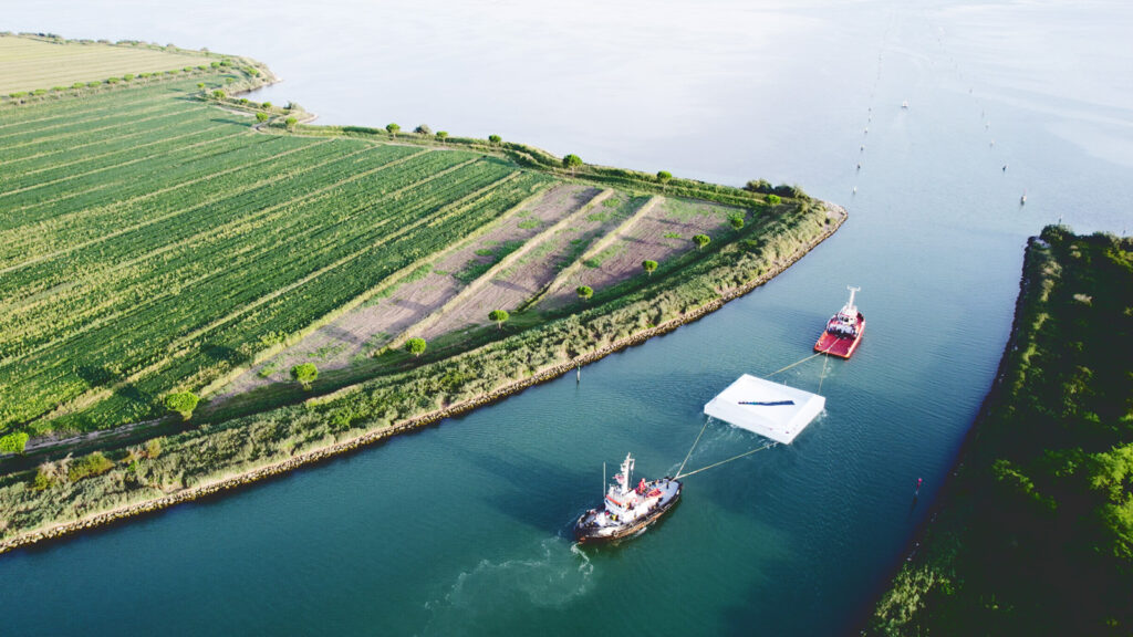 The AquaPraça exhibit is towed by two boats through a canal