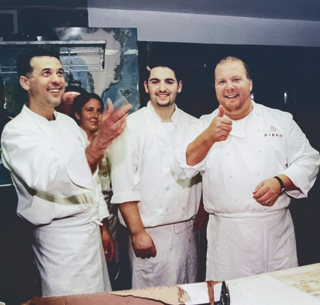 Laurie Woolever behind three men in a restaurant kitchen. Mario Batali is at right.