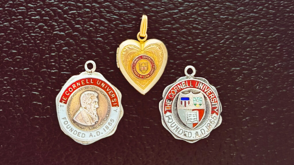three vintage pendants show iterations of the Cornell insignia over time
