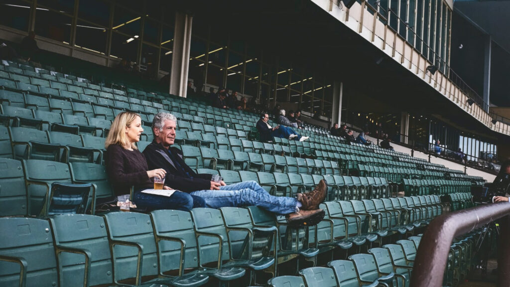 Laurie Woolever and Anthony Bourdain sitting in a near-empty stadium