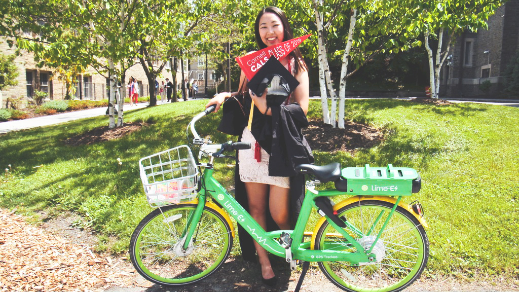 Michelle Shin with a green bicycle holding Commencement swag