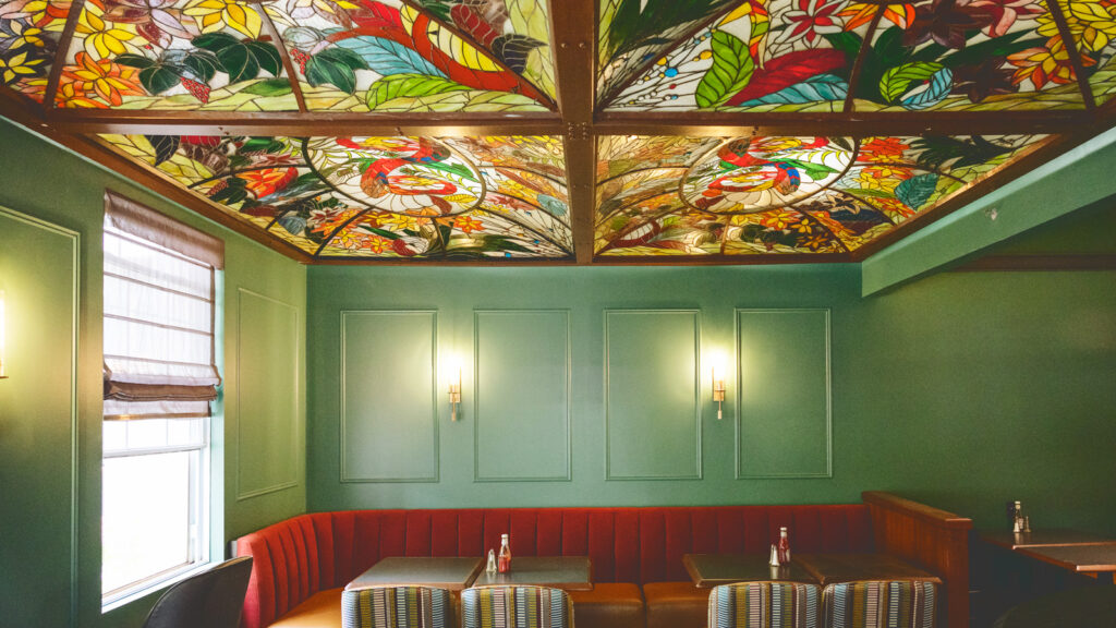 A restaurant seating area with a colorful glass ceiling, green walls and red banquettes