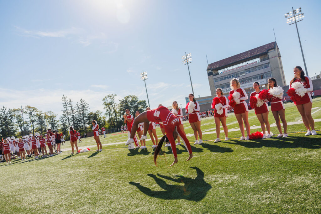 A cheerleader mid back handspring while other cheerleaders watch in the background holding their pompoms at Schoellkopf Field.