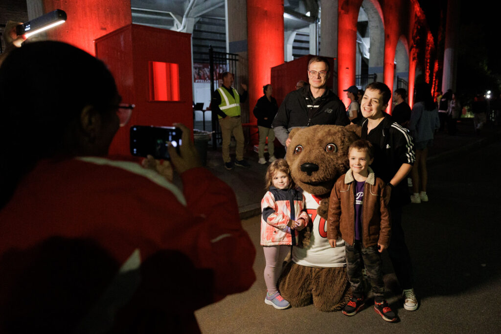 A family smiles for a photo with Touchdown outside of Schoelkopf Field before the drone and laser show.