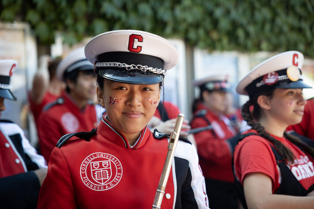 A flute player in uniform in the Big Red Band smiles while holding her flute to the side of her.