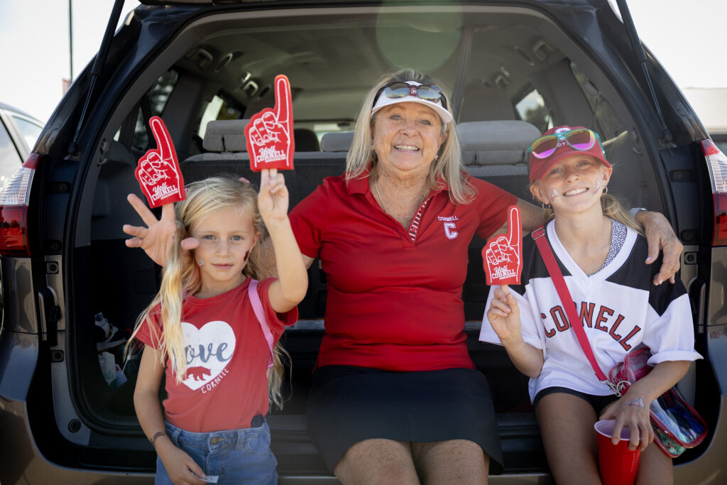 A woman poses with two children in the back of their car as they all show off their red Cornell foam fingers during the tailgate.