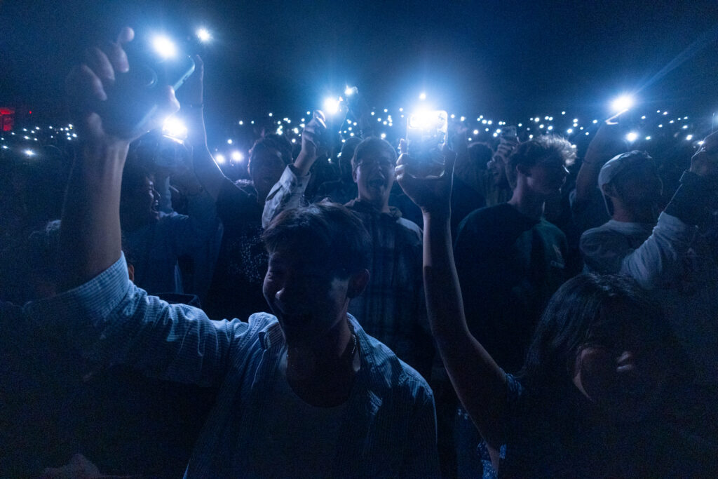 Spectators hold there phone flashlights over their head in the dark at Schoellkopf Field during the drone and laser show.