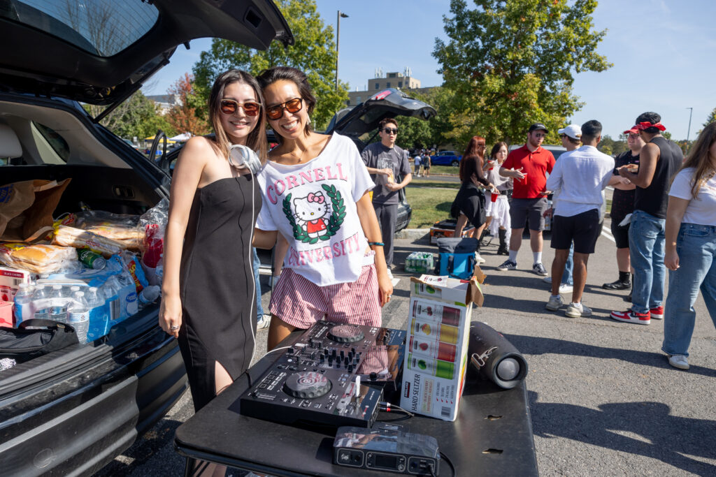 A DJ smiles with an attendee in front of her equipment with headphones around her neck during the tailgate before the homecoming game.