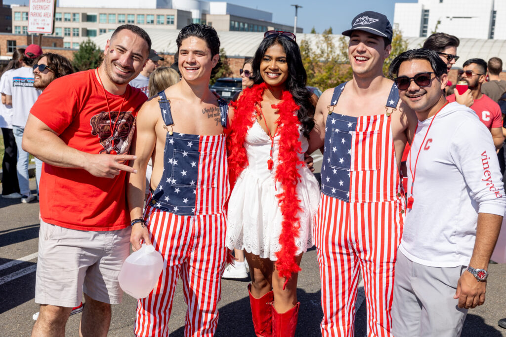 Five students smile for a photo while wearing Cornell and American flag apparel on campus during homecoming.