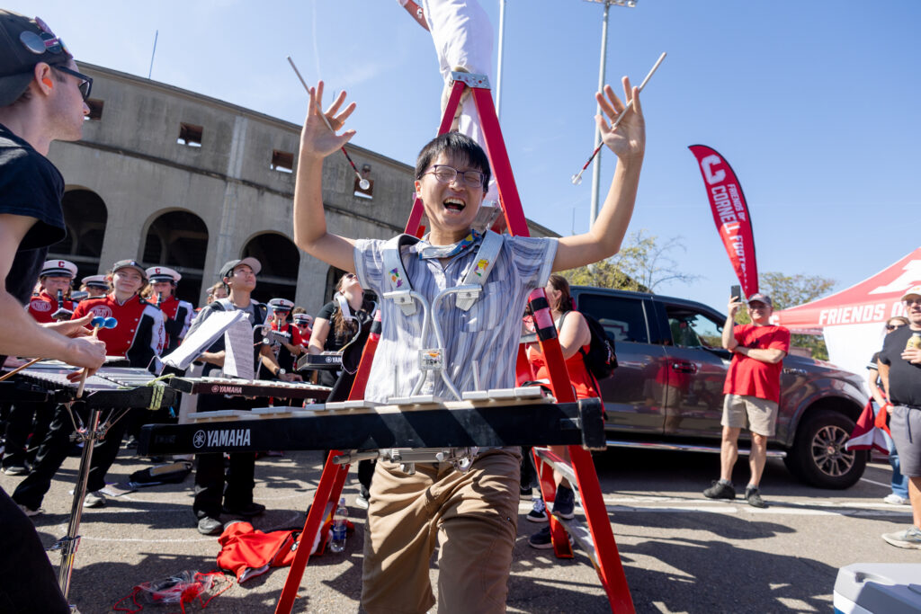 A member of the Big Red Band plays the xylophone and holds the mallets up and smiling.