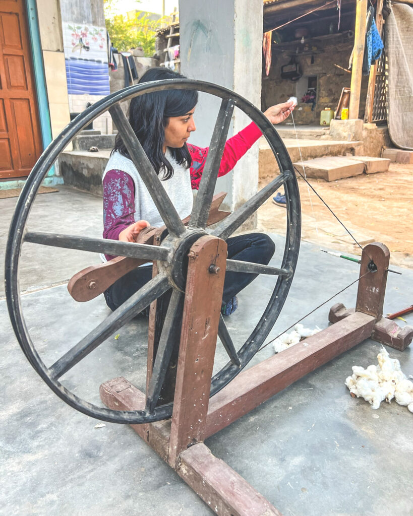 Aishwarya Lahariya learning how to hand spin yarn from a large wooden and medal wheel.