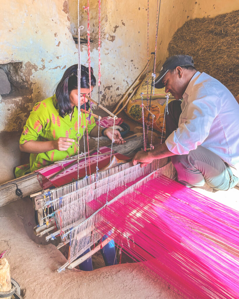 Aishwarya Lahariya learning how to use a loom to weave pink yarn from an artisan.