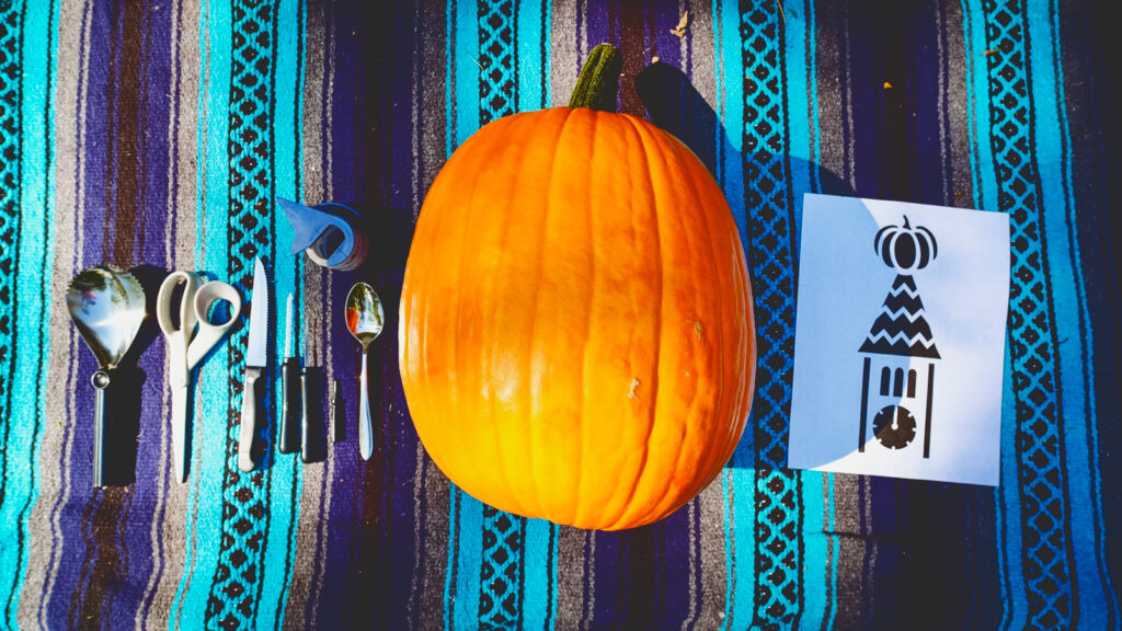 pumpkin, paper stencil, and carving tools laid out on a blanket