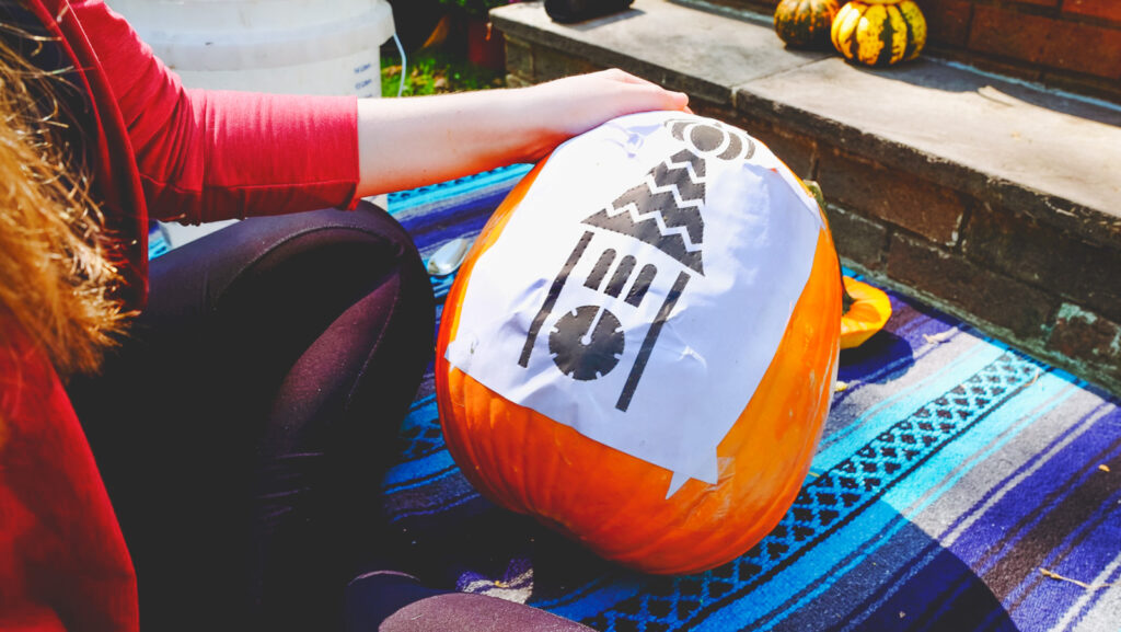 pumpkin with paper stencil taped on it after holes have been poked along the outlines of the design