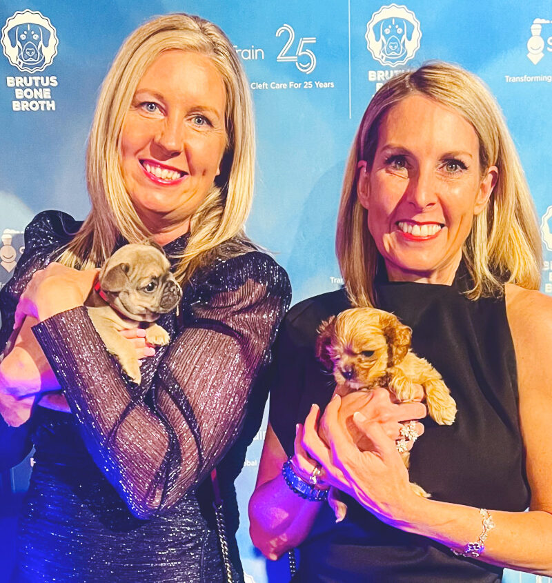 Kim Hehir with her sister holding puppies at an event for SmileTrain that Brutus Bone Broth sponsored.