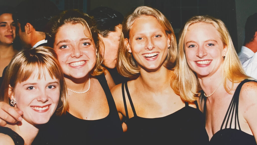 Megan Overbay as a student with friends smiling while all wearing black dresses.