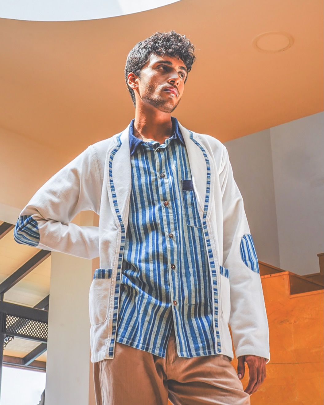 A male model for Jiwya wears a blue striped, collared shirt and a white jacket with matching stripes on the trim.