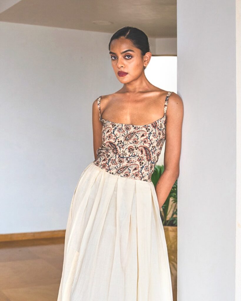 A model stands in a doorway wearing a Jiwya dress that features a floral pattern at the top and a white, flowy skirt.