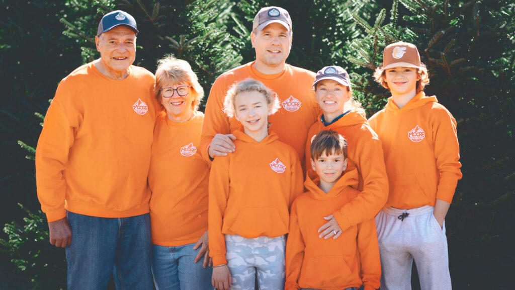 Jason Moore with his wife, kids, and parents all wearing orange Moore Family Farm clothing in front of Christmas trees.