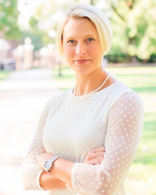 Megan Overbay smiling in a white long sleeve blouse and peal necklace outdoors.