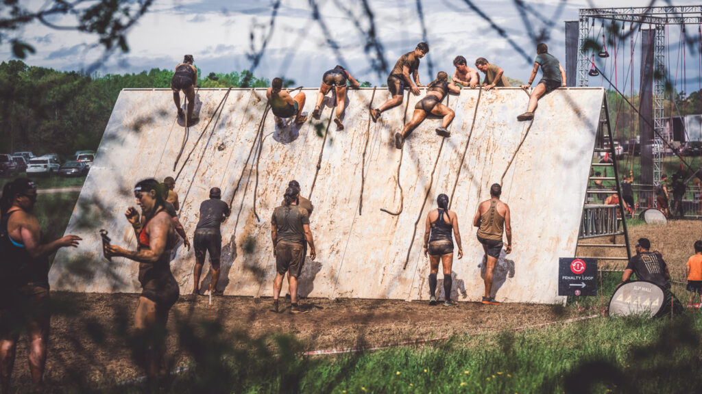 Participants take turns pulling themselves over a slanted wall with a rope.